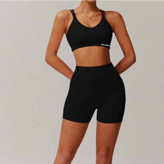 Person wearing a black sports bra and high-waisted shorts on a plain background