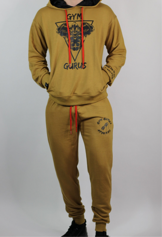 A man wearing a gold French terry jogger set with 'GYM GURUS' embroidered on the front, including matching pants and a hoodie with a visible logo.